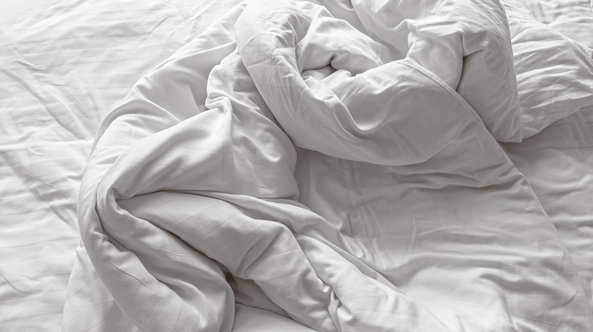 an unmade bed with white sheets and pillows