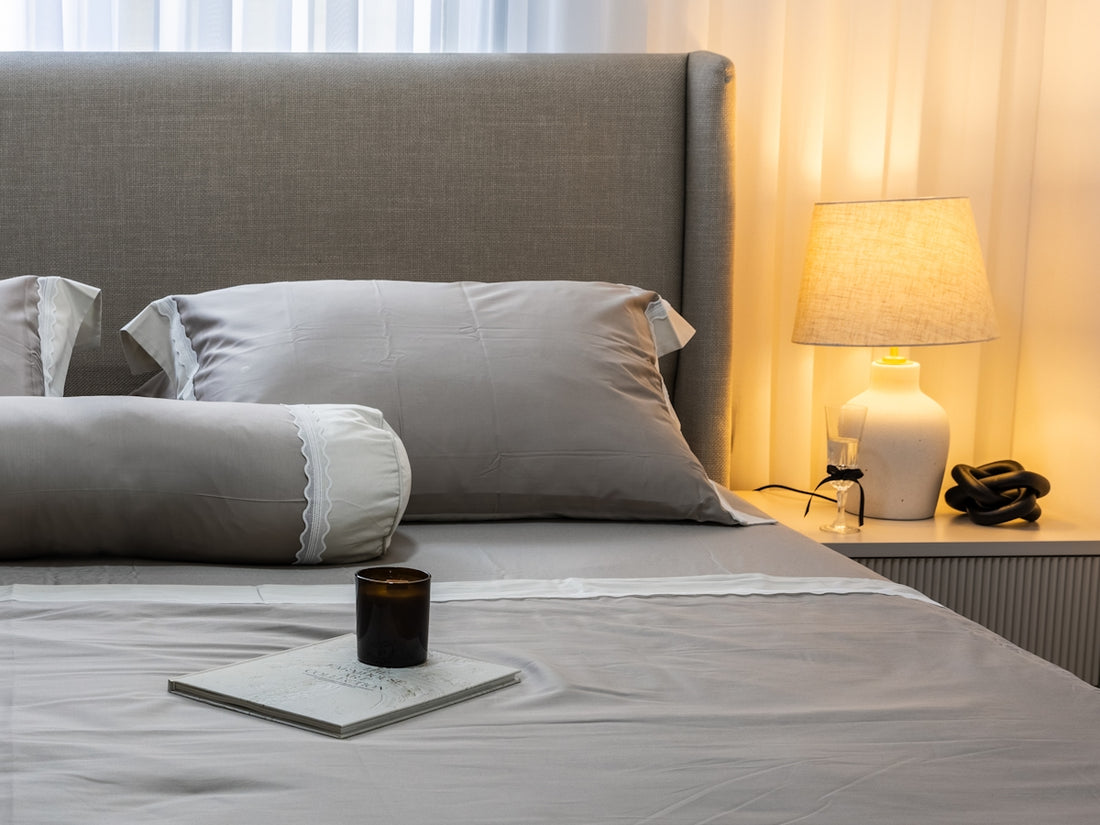 A neatly made bed with grey linens and pillows.