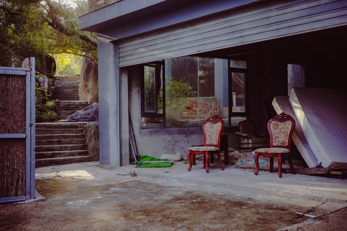 Two ornate chairs sit in a dusty garage entrance