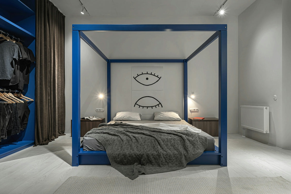 A blue canopy bed with a grey knit blanket in a modern bedroom