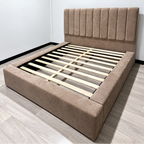 A low-profile platform bed frame upholstered in a Mink Plush fabric, featuring a tall, vertically channel-tufted headboard and light-colored wooden slats, shown in a minimalist bedroom setting.