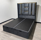 Angled view of the grey Luxe Panel Ottoman Bed with padded geometric headboard and gold trim